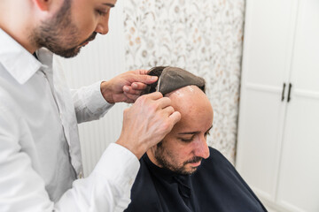 Hairdresser combing a hair replacement system on a balding man's head in a hair clinic, offering a...