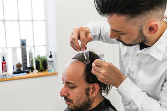 Hairdresser applying glue on hair system for man customer in a hair salon, hair replacement procedure for alopecia and baldness treatment