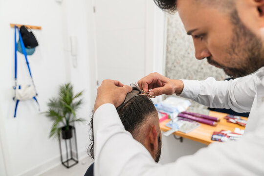 Hair clinic specialist attaching hair replacement system to client, offering solution for hair loss and boosting self confidence