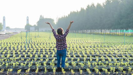 Young woman celebrating success with raised arms in the middle of green plant nursery field, symbolizing freedom, agriculture, growth, and sustainable farming
