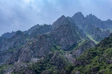 A close-up of mountain peaks, covered in some places with green vegetation, in cloudy weather, when...