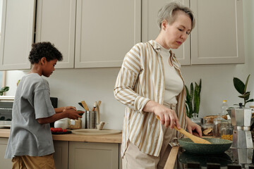 Woman and child preparing meal in contemporary kitchen with various ingredients and appliances, showcasing teamwork and family bonding