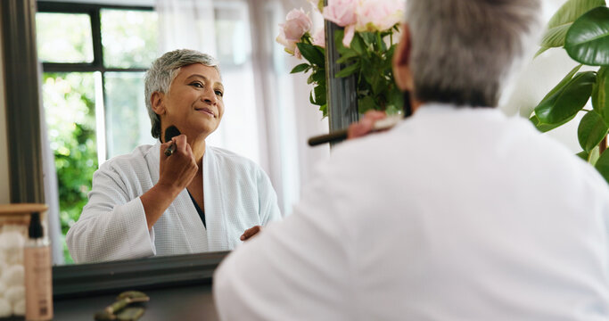 Woman, brush and mirror in home with makeup, concealer and cosmetics in bedroom. Mature person, getting ready and smile in reflection for skincare, beauty procedure and powdering skin at vanity table