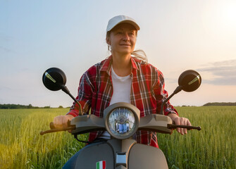 Woman riding a scooter through a lush green field during sunset in a tranquil rural setting