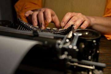 Hands typing on a vintage typewriter in a dimly lit workspace with a focus on the creative process