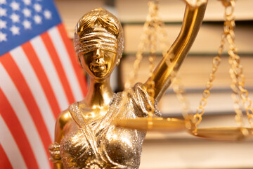 Statue of Lady Justice holds scales in front of books and American flag symbolizing law and order...