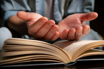 Engaged in reading an open book with hands raised in contemplation or prayer during evening time