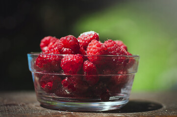 Transparent plate with juicy sweet raspberries on wooden table