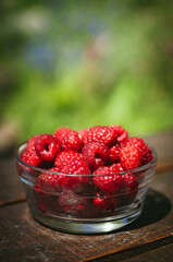Transparent plate with juicy sweet raspberries on wooden table