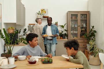 Smiling multi-ethnic family sharing breakfast in cozy kitchen. Healthy food and plants creating warm, inviting atmosphere