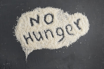 No Hunger text written on a rice scattered on a dark table. Food crisis, global hunger, food supply...