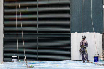Real life worker labour painter construction worker climbing up hanging on wall painting the building wall