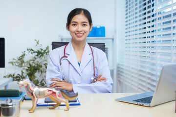 A confident Asian female veterinarian sits at her desk, providing online consultations. She uses...