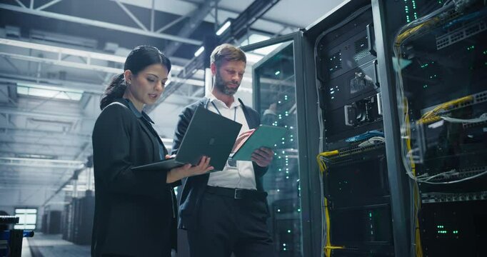 Female Data Center System Administrator and Male IT Specialist Talking in Server Room and Using Laptop and Tablet Computers. Information Technology Engineers Working on Artificial Intelligence Network