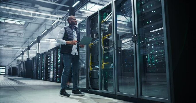 Data Center: African Programmer Using Laptop Computer, Focused while Inputting Data. Cloud Computing Server Farm System Administrator Working on IT Maintenance for Saas Business Company