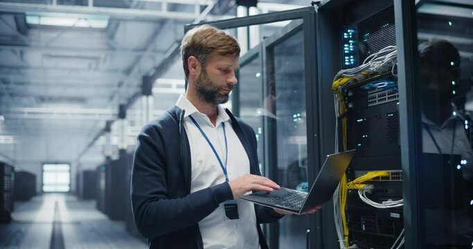 Portrait of a Data Center Engineer Using a Laptop Computer. Handsome Man Looking at Camera and Smiling. Information Technology Specialist Standing in a Facility with Operational Server Racks - Powered by Adobe