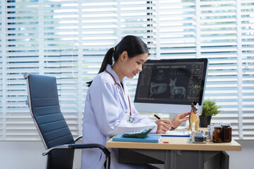A confident Asian female veterinarian sits at her desk, providing online consultations. She uses...