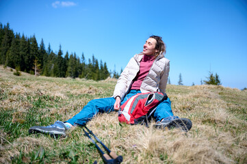Female sitting on the hill of high mountains enjoying summer nature scenery. A girl siting on the edge of the cliff and looking at the sun valley and mountains. Happy traveler enjoying sunny day