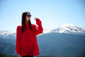Hiker girl on background of snowy mountains. Young female in red sport jacket and sunglasses hiking in the mountains. Incredible landscape reflects peace and freedom.