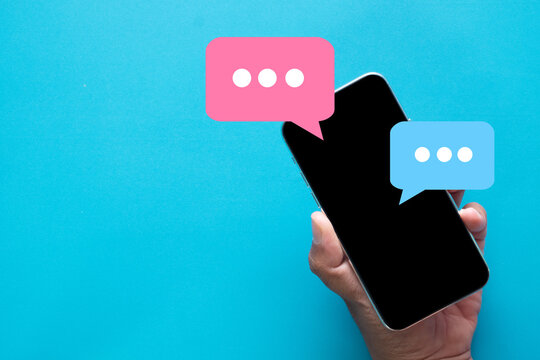 Hand holding a smartphone with pink and blue chat bubbles. Concept for online messaging apps,digital dialogue,social media communication,and instant messaging.Blue background with copyspace.