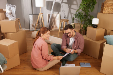 A couple sits on the floor of their new home, reviewing documents while surrounded by moving boxes...