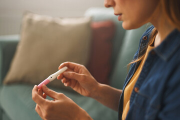A woman rests on a sofa, intently examining the results of a pregnancy test. The room is warmly lit, with colorful cushions in the background adding to the atmosphere.