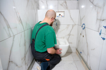 Plumber installing toilet. Modern toilet installation. Worker installing a wall-hung toilet on the...