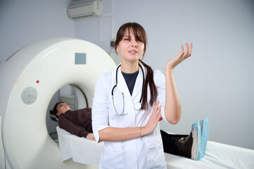 Young female radiologist staying in CT scanning room. Working in the clinic. Pretty doctor looking...