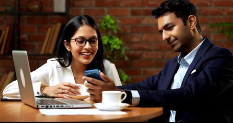 Indian business people using smartphone in office break, closeup of Asian corporate man and woman in professional attire casually scrolling social media or photos on phone while seated in cozy office - Powered by Adobe