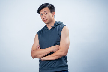 Asian man standing with arms crossed, wearing a dark sleeveless hoodie and navy pants, posing...