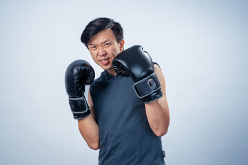 Asian man in sleeveless hoodie wearing boxing gloves strikes forward fighting pose with intense...