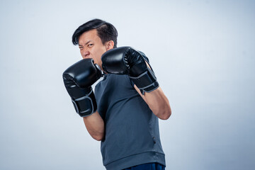 Asian man in sleeveless hoodie wearing boxing gloves strikes forward fighting pose with intense...