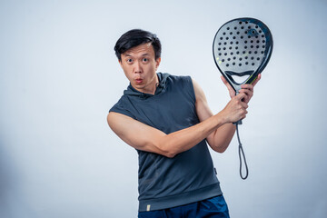 Asian man in sleeveless hoodie holding black padel racket with both hands in mid-swing position,...