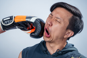 Asian man in sleeveless hoodie gets punched in the face with boxing glove during training, showing...