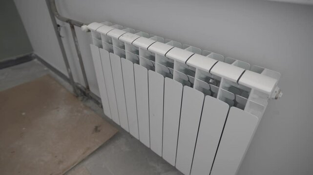 Shiny bimetallic radiator fixed below window stands out against bare concrete wall. Functional unit awaits connection in half-finished room