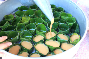 Pouring Palm Sugar Mixture for Thai Dessert. alm sugar filling is poured into green banana leaf...