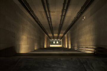 Indoor shooting range showing paper targets suspended at end of long tunnel, empty firing lane, no...