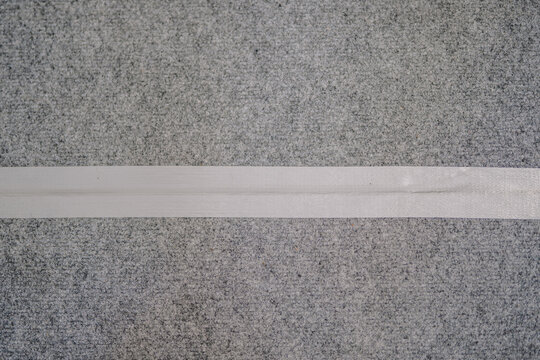 Close-up of a strip of white duct tape adhered to a textured grey carpet or felt surface, positioned horizontally across the frame.