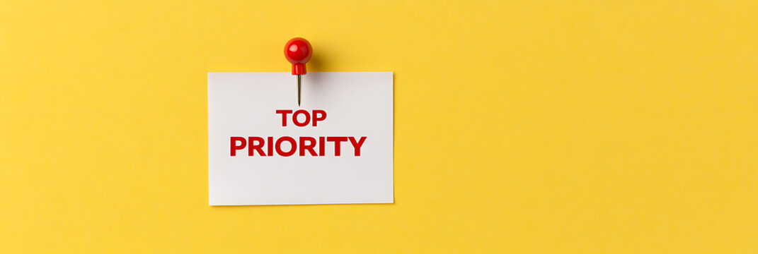 Note with text "Top Priority" pinned to a yellow background. Visual representation of importance and focus on crucial tasks. Time management. Urgency.