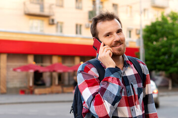 Smiling young man talking on phone in urban setting. Guy talking on smartphone outdoors. Concept of...