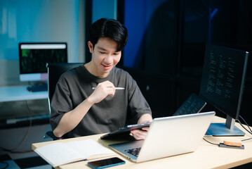 Asian male programmer working with tablet, laptop, and desktop in tech office. Coding, software...