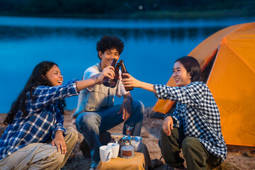 Three people are sitting around a campfire, drinking beer and laughing. Group of friends enjoy outdoor camping, a celebration of friendship, connection, and togetherness around a campfire.