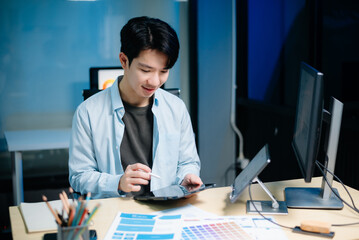Asian UX,UI designer reviewing app wireframes and color samples in modern office. Creative process,...