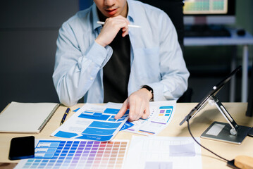 Asian designer’s hands reviewing UX/UI mockups and color palettes at modern desk. App design,...