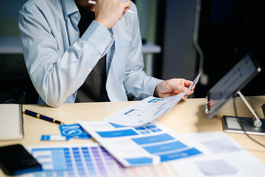 Asian designer’s hands reviewing UX/UI mockups and color palettes at modern desk. App design, user interface