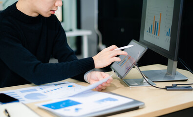 Closeup of young Asian professional analyzing business charts on a tablet with stylus. Concept of...