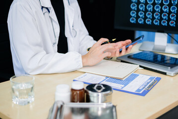 Asian doctor studying brain MRI scans on monitor and writing notes in modern clinic. Concept of...