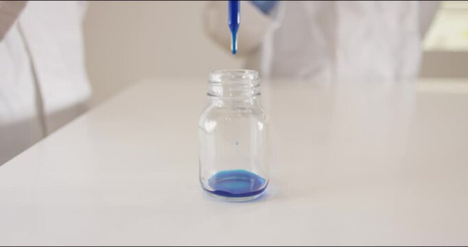 Sample drops of blue ink are poured into a glass by scientists with a pipette in a laboratory