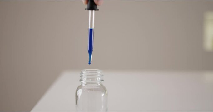 Sample drops of blue ink are filled into a small glass by scientists with a pipette in a laboratory