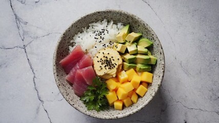 A colorful poke bowl featuring sushi rice, fresh tuna, avocado, mango, and garnished with sesame seeds and cilantro. Perfect for National Hawaii Day..